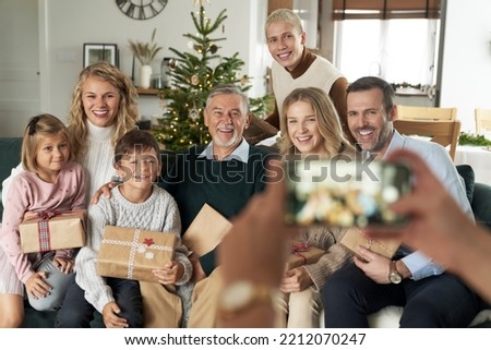 Unrecognizable caucasian person taking picture of family sitting on sofa and holding Christmas presents