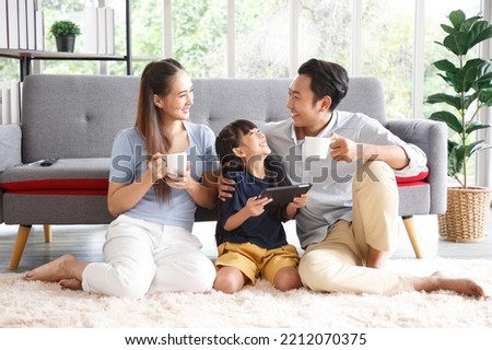 Happy young asian family mom and dad with daughter having fun in liviing room at home, while daughter using tablet. Family,love and happiness concept.