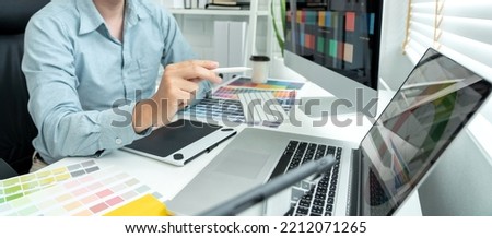 Male graphic designer is choosing color swatch samples on multiple screens and sketching on tablet digital to working graphic design with technology in modern office.