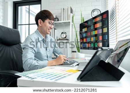 Male graphic designer is choosing color swatch samples on multiple screens and sketching on tablet digital to working graphic design with technology in modern office.