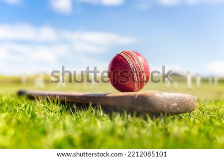 Cricket ball on top of old wooden cricket bat on green grass of cricket ground background Royalty-Free Stock Photo #2212085101
