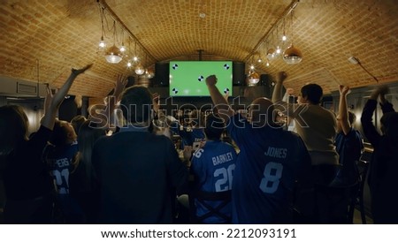 WIDE Model released, fans watching a game on a large TV in a sport pub, celebrating a goal, green screen chroma key Royalty-Free Stock Photo #2212093191