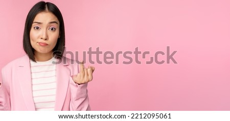 Portrait of young asian business woman, saleswoman shrugging shoulders and looking confused, clueless of smth, standing over pink background