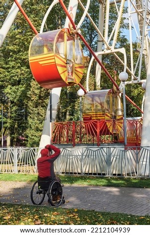 a photographer in a wheelchair takes pictures of the ferris wheel attraction in a city park