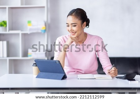 Asian Woman using digital tablet while sitting at home workplace, Asian Female designer sketching on a graphic tablet while working at home.