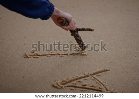Close up on a woman's hand writing a message in the sand with a wooden stick. Vignetting around the hand on which the focus is made. Tilt shift effect.