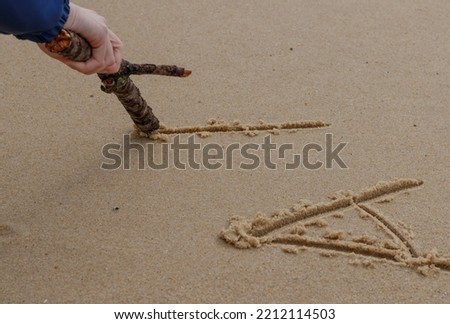 Close up on a woman's hand writing a message in the sand with a wooden stick. Vignetting around the hand on which the focus is made. Tilt shift effect.