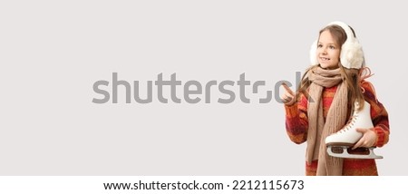 Cute little girl with ice skates pointing at something on light background with space for text