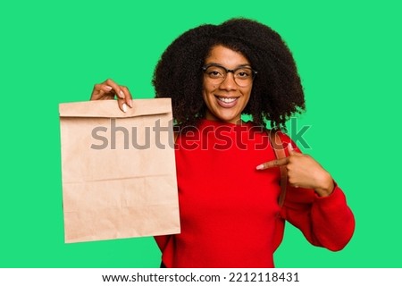 Young African american woman holding take away food isolated person pointing by hand to a shirt copy space, proud and confident Royalty-Free Stock Photo #2212118431