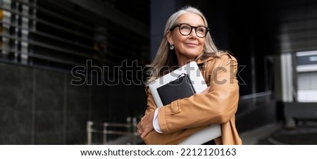 portrait of an elderly businesswoman with a laptop in glasses outside the office, strong and independent woman concept Royalty-Free Stock Photo #2212120163