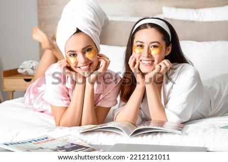 Beautiful young women with under-eye patches reading magazine in bedroom