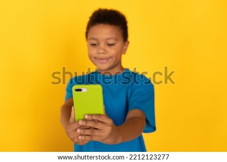 Smiling preteen boy wearing blue T-shirt boy using smartphone. Portrait of multiethnic child playing or surfing internet on cellphone. Social networking and technology concept