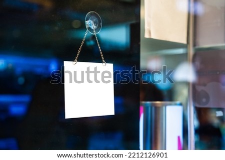 Empty white plastic signboard hanging on glass window in shopping store
