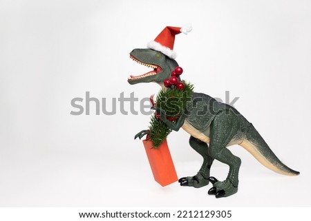Toy green predator dinosaur in a Christmas hat with a bag and a Christmas tree on a white background. Concept: Christmas, gifts, shopping, buyer, black Friday, sales, winter weekend