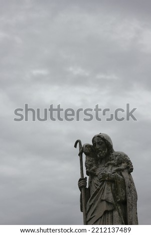 Worn and weathered stone statue of Jesus Christ carrying a small limb on his shoulders.