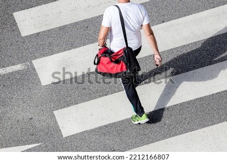 Scene of a unrecognizable man wearing sportswear and carrying a gym bag walking on a zebra crossing on his way to a sports center. High angle view
