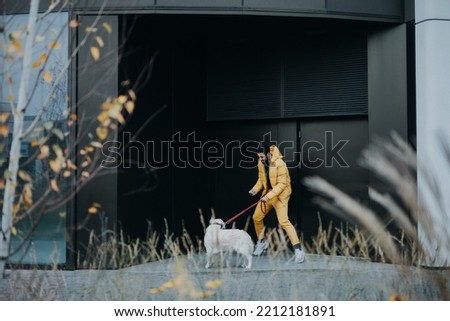 Happy young man walking his dog outdoors in city during autumn day.