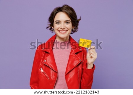Young smiling happy rich satisfied woman 20s wear red leather jacket hold in hand credit bank card isolated on plain pastel light purple background studio portrait. People lifestyle fashion concept