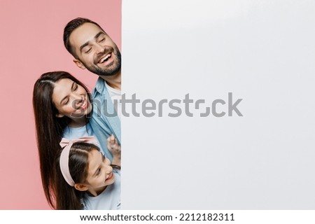 Young parents mom dad with child kid daughter teen girl in blue clothes hold big empty billboard for promotional content, place area for text or image isolated on plain pastel light pink background.