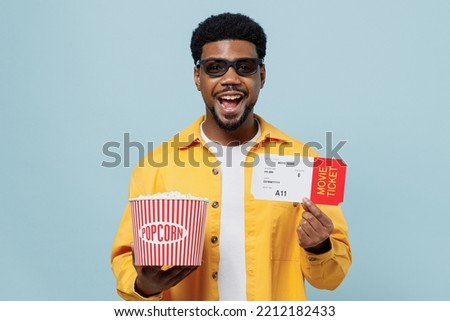 Young smiling man of African American ethnicity in 3d glasses watch movie film hold bucket of popcorn ticket look camera isolated on plain blue background People emotions in cinema lifestyle concept Royalty-Free Stock Photo #2212182433