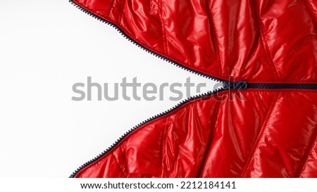 Open blue zipper on red winter down jacket on light background with copy space