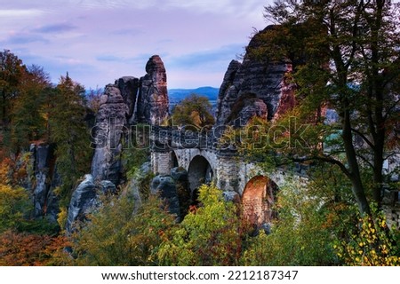 Amazing autumn landscape in Saxon Switzerland National Park. View of The Bastei Bridge is a rock formation, exposed sandstone rocks and forest hills at sunset. Germany. Saxony. Royalty-Free Stock Photo #2212187347
