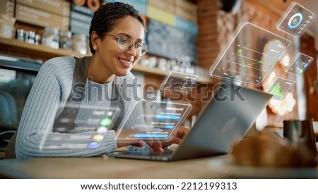 Beautiful Latina Coffee Shop Owner is Working on Laptop Computer and Checking Inventory in a Cozy Cafe. Restaurant Manager Browsing Internet and Chatting with Friends. VFX Augmented Reality Concept. Royalty-Free Stock Photo #2212199313