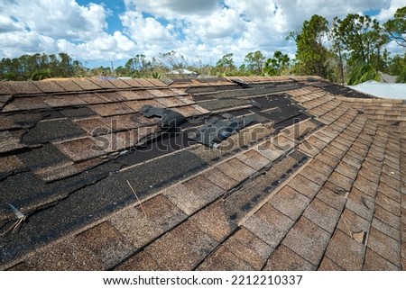Damaged house roof with missing shingles after hurricane Ian in Florida. Consequences of natural disaster Royalty-Free Stock Photo #2212210337