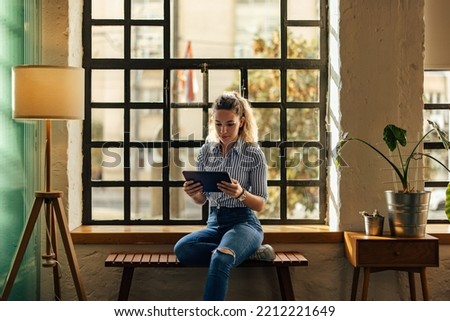 Focused girl working over the tablet, siiting next to the window, at the office. Royalty-Free Stock Photo #2212221649