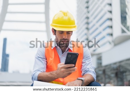 Man engineer sitting on construction site. construction manager using walkie talkie. Engineer working on outdoor project and talking on phone Royalty-Free Stock Photo #2212231861