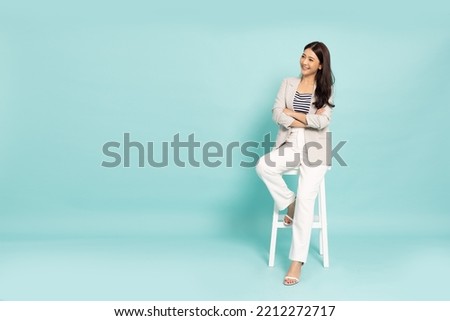 Portrait of successful business asian woman smiling and sitting on white chair isolated over green background, Full length composition Royalty-Free Stock Photo #2212272717