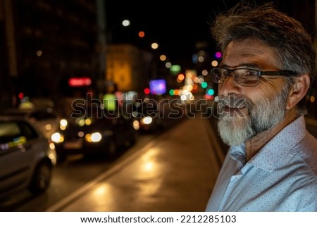 Portrait of Handsome Mature Man Smiling, Looking at Camera, Standing in Night City with Bokeh Neon Street Lights in Background. Happy Confident Mature Man with Stylish Hair. Close-up Portrait