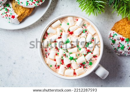 Cup of hot chocolate or cocoa with marshmallows and colored sprinkling and glazed cookies, top view. Festive Christmas background with fir tree.