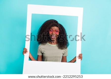 Photo of adorable excited lady wear striped t-shirt arm dark glasses holding paper photo frame isolated turquoise color background