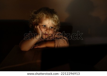 Portrait of a cute child. a girl watches a tablet with cartoons or a movie in the evening. Lamp light in the room.