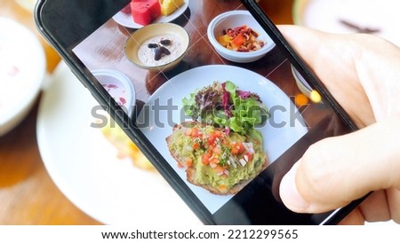Man hands taking photos of healthy vegan breakfast or dinner food by smartphone. Male person holds mobile phone and shooting his food for social network. Blogger in restaurant make content