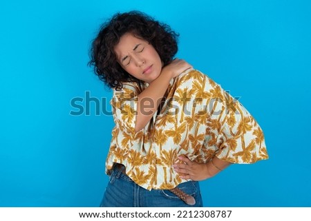 brunette arab woman wearing hawaiian shirt over blue background got back pain