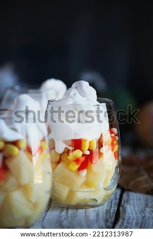 Halloween parfait made from layers of chopped pineapples, candy corn, and whipped cream. Selective focus with pumpkins and leaves in  blurred background.  