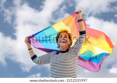 Older lady waving the rainbow colored flag representing the gay community. Gay Pride Day. Fight for equality, freedom and rights for gays, lesbians, trans and non-binary people Royalty-Free Stock Photo #2212331997
