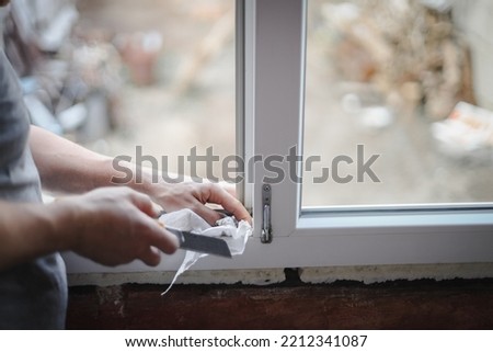 A caucasian man washing his hands with a dry paper napkin using a construction knife inside a window frame opening, close-up side view with selective focus. The concept of home renovation