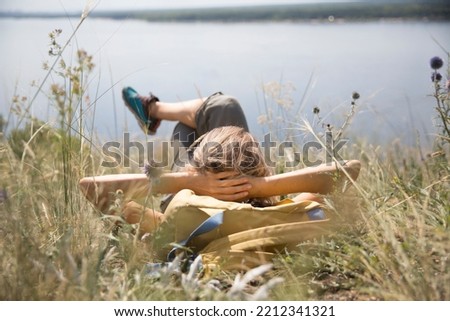 middle aged woman with a backpack  rests on the grass outdoor. copy space. Slow life. Enjoying the little things. spends time in nature in summer. Lykke concept Royalty-Free Stock Photo #2212341321
