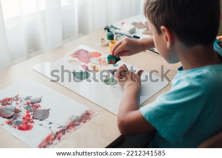 Cute child sitting at desk and making picture from dry birch leaves. Autumn activities for children