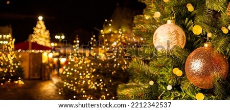 European Christmas city with festive fair or market in the evening. Christmas tree with beautiful balls on foreground. Holiday background.