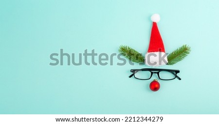 Face of a reindeer with a red bauble nose, fir antlers, a santa claus hat and eyeglasses, merry christmas greeting card
