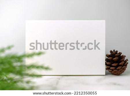 Minimal style blank white greeting card on white marble floor for fill the blessing in celebrating the festival of love and happiness with blurry green leaves foreground