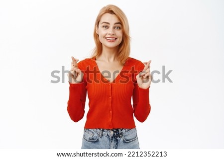 Smiling hopeful girl with crossed fingers, waiting for dream come true, wishing, standing over white background