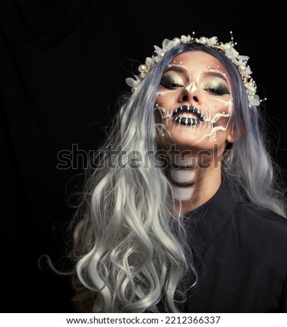 Halloween. Portrait of young beautiful girl with make-up skeleton on her face. Black background