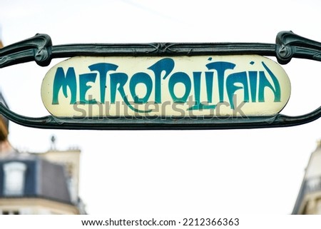 Sign with the subway logo (yellow and green symbol) in front of a parisian metro (metropolitain) station with a blue sky in the background during a summer day in Paris, France