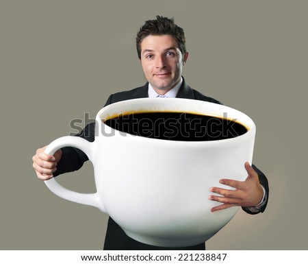 young happy business man holding a funny huge and oversized cup of black coffee in caffeine addiction concept isolated on even background