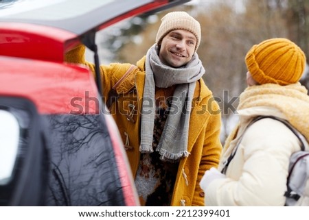 Portrait of smiling young couple standing by car arriving for winter vacation